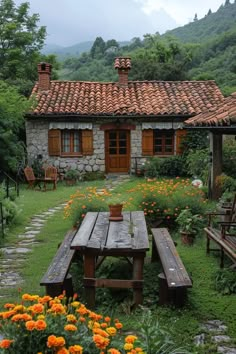 a wooden table sitting in the middle of a garden next to a stone building and flowers