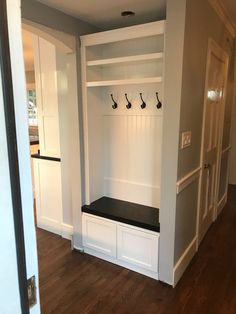 an empty room with white cabinets and black bench in the center, along with several coat hooks on the wall