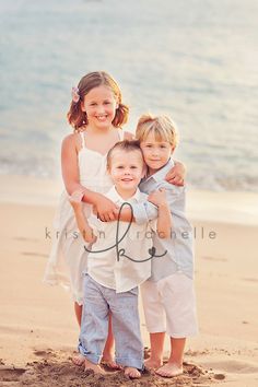 three children standing on the beach with their arms around each other