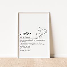 a white framed poster with the words surfer on it in front of a wooden floor