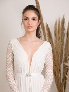 a woman wearing a white dress standing in front of some tall grass and dried plants