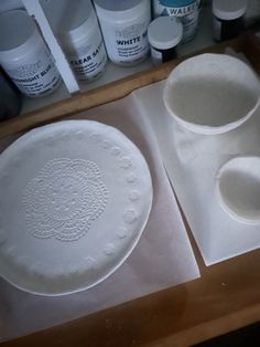 two white dishes sitting on top of a wooden table next to paint bottles and paper towels