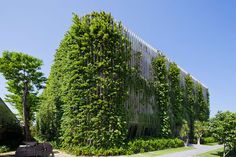 the building is covered in green plants and has many trees on it's sides