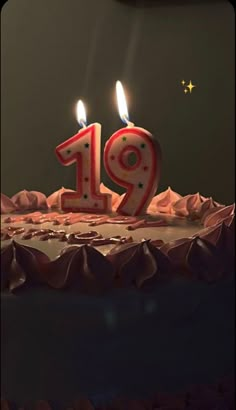 a birthday cake with two lit candles in the shape of number 19 on it's frosting