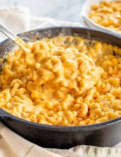 a skillet filled with macaroni and cheese being stirred by a ladle