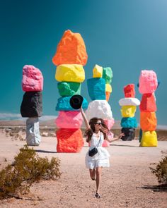 a woman in a white dress is running by some colorful sculptures on the desert road