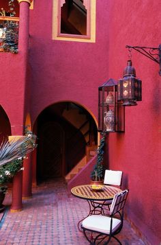 an outdoor patio with tables and chairs in front of a pink wall, surrounded by potted plants