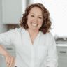 a woman standing in a kitchen with her hands on the counter and smiling at the camera