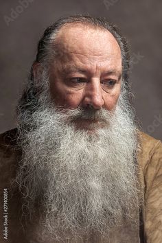 an old man with a long white beard wearing a brown shirt and looking at the camera