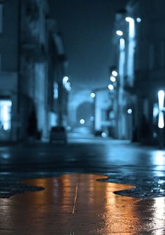 an empty city street at night with rain on the ground and buildings in the background