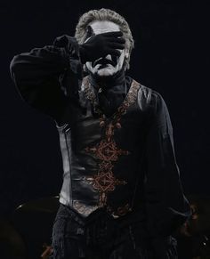 a man with his face painted black and wearing a mask, standing in front of a dark background