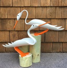 two white storks are standing on wooden posts next to a brown brick wall