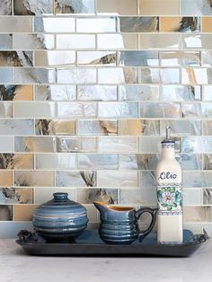 there is a teapot and two cups on the counter in front of a mosaic tile backsplash