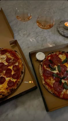 two pizzas sitting on top of cardboard boxes next to glasses of wine and candles