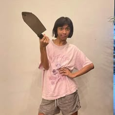 a woman holding a large knife in her right hand and posing for the camera while standing next to a white wall