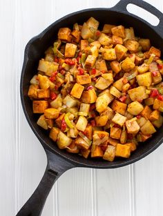 a skillet filled with cooked vegetables on top of a white wooden table next to a spoon