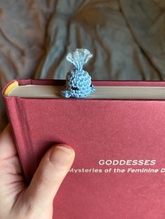 a hand holding a red book with a tiny blue bunny on top