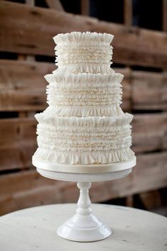 a three tiered white cake on top of a round table with wooden pallets in the background