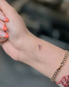 a woman's arm with an orange manicure and a small tattoo on it