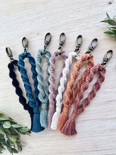 six different colors of key chains with tassels on top of each one and some greenery in the background