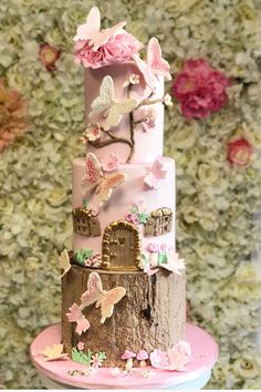 a three tiered cake decorated with pink flowers and butterflies on a table in front of a floral wall