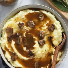 mashed potatoes topped with mushrooms and gravy in a pan next to a wooden spoon