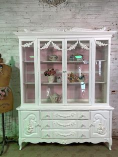 a white china cabinet sitting next to a mannequin in a room with brick walls