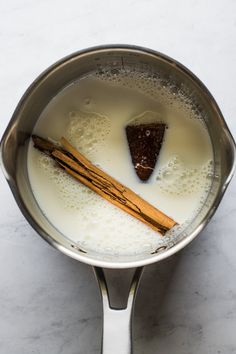 cinnamon sticks and milk in a saucepan on a marble counter top with white background