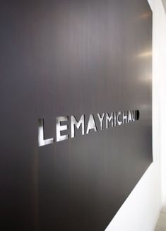 the entrance to lemaymichau is shown in black and silver letters on a white wall