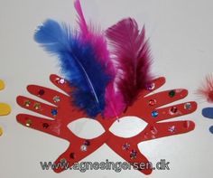 a red mask with feathers on it next to other colorful decorations and magnets in the shape of hands