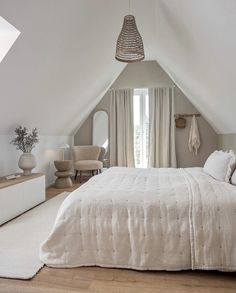 an attic bedroom with white walls and wood flooring is furnished with natural light from the windows