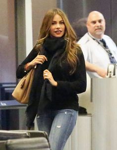 a woman walking through an airport carrying a brown bag and wearing ripped jeans, black sweater and boots