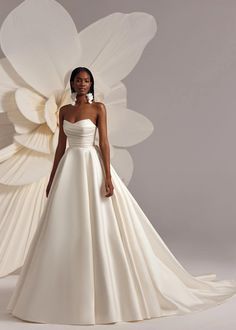 a woman in a white wedding dress standing next to a large flower shaped object with petals on it