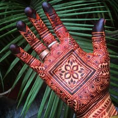 a person's hand with henna tattoos on it and palm leaves in the background