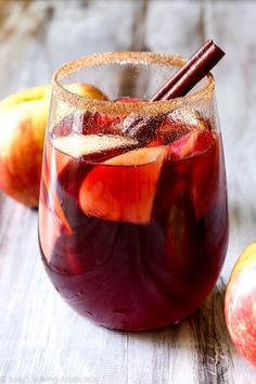 a glass filled with liquid next to an apple and cinnamon stick on top of a wooden table