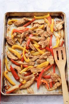 chicken fajita with peppers and bell peppers on a baking sheet next to a wooden spatula