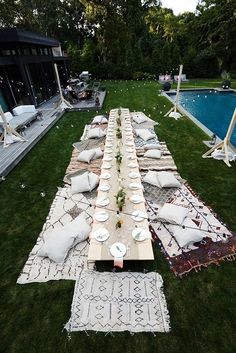 a long table set up with plates and napkins in the grass near a swimming pool