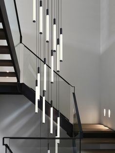 a modern staircase with glass railings and lights hanging from it's sides, leading up to the second floor