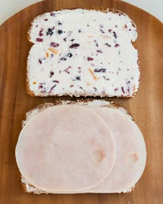 two slices of bread with white cheese and cranberry toppings on them sitting on a wooden plate