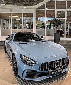 a blue mercedes sports car parked in front of a building with glass doors and windows