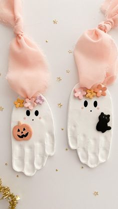 two handprinted ghost ornaments with gold glitters on the side and one wearing a pink hat