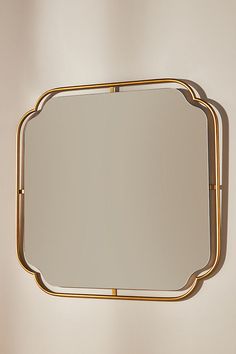 a square mirror hanging on the wall with gold trimmings and a metal frame