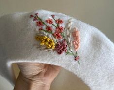 a hand holding a white hat with flowers on it