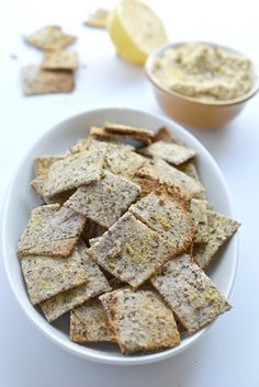 a white bowl filled with crackers next to lemon wedges