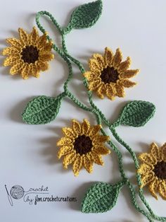 three crocheted sunflowers with green leaves and brown centers on white background