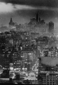 an old black and white photo of the city skyline at night with clouds in the sky