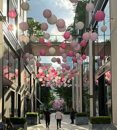 two people walking down a street with pink and white lanterns hanging from the ceiling above them