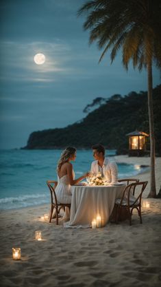 a man and woman sitting at a table on the beach with candles in front of them