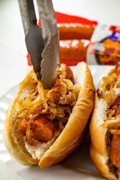 two hot dogs on buns with onions and ketchup being cut by a knife