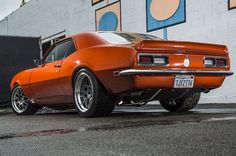 an orange muscle car parked in front of a building